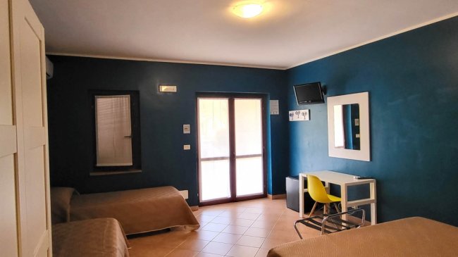 Camera con due letti, scrivania e sedia gialla.