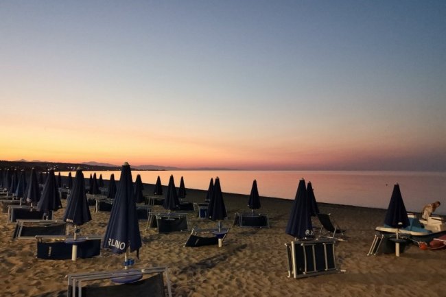 Una spiaggia al tramonto con ombrelloni blu scuri chiusi.