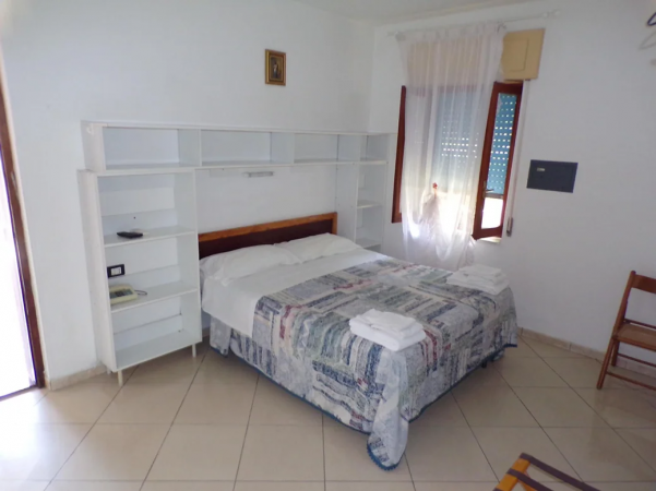Una camera con letto matrimoniale, coperte colorate, mensole e finestra con tende.