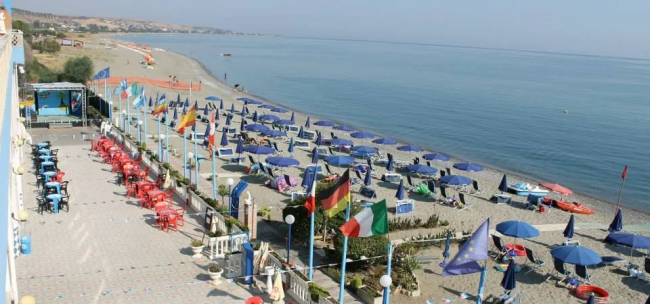 Spiaggia con ombrelloni blu e sedie rosse vicino al mare.