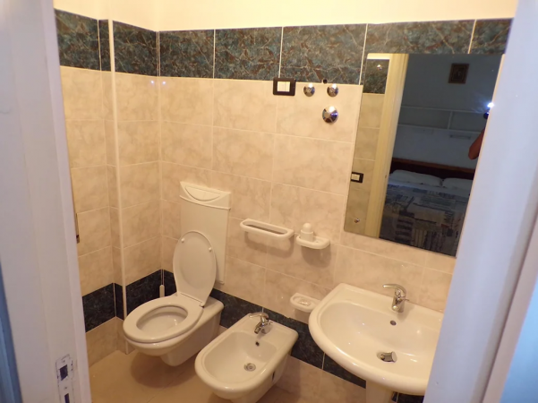 Un bagno con WC, bidet, lavabo e ampio specchio su pareti piastrellate.