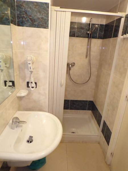Bagno con doccia, lavabo e asciugacapelli a parete, piastrelle scure e chiare.