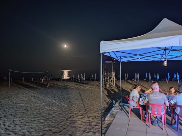 Spiaggia di notte con gazebo e persone sedute.