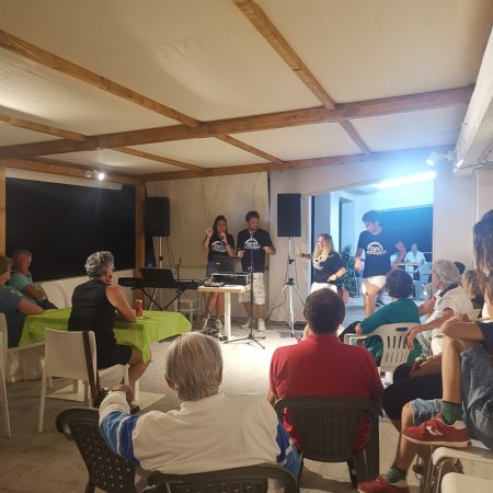 Evento al chiuso con persone sedute e presentatori in piedi.