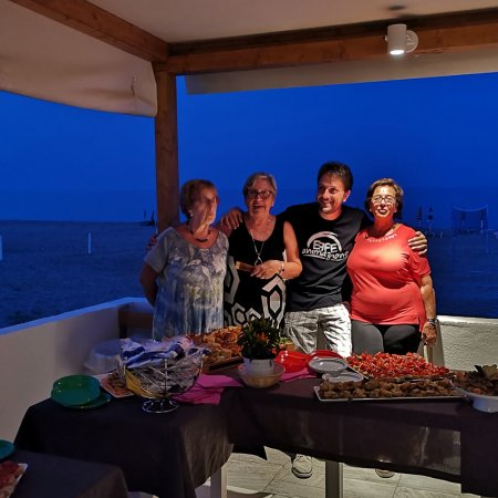 Quattro persone sorridenti al tavolo all'aperto con cibo.