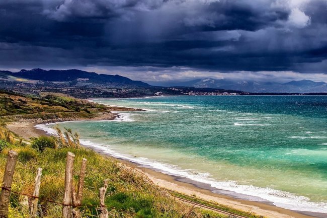 Costa con mare mosso sotto cielo nuvoloso.