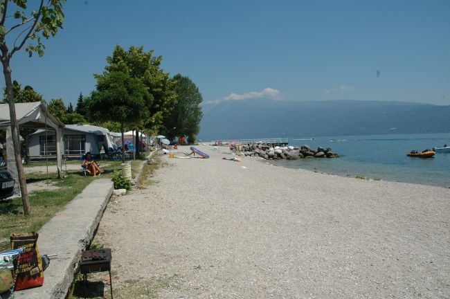 Spiaggia di ghiaia con tende da campeggio vicine e vista su un lago.
