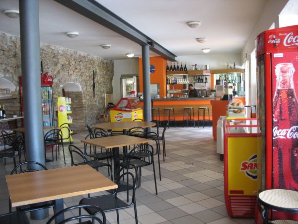 Un bar accogliente con tavoli e sedie nere, bancone arancione e frigo Coca-Cola.