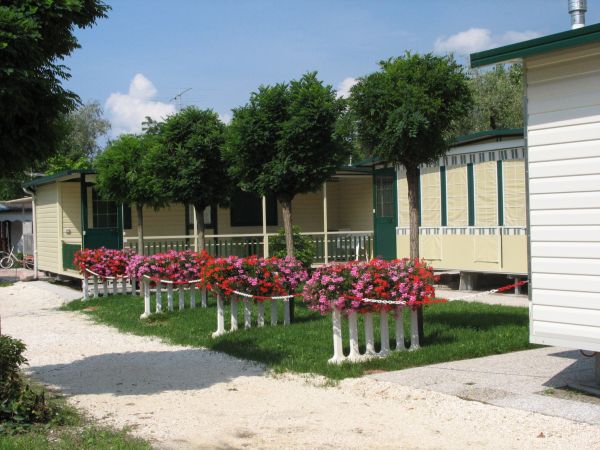 Mobilhome con terrazza fiorita, alberi e vialetto di ghiaia.
