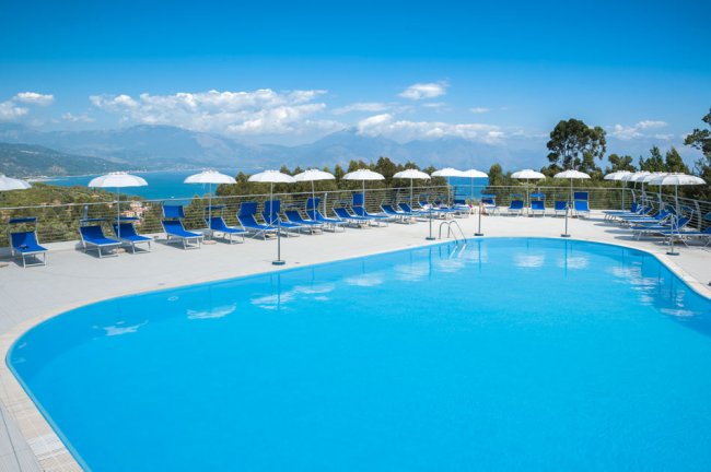 Piscina grande con lettini blu e vista mare.