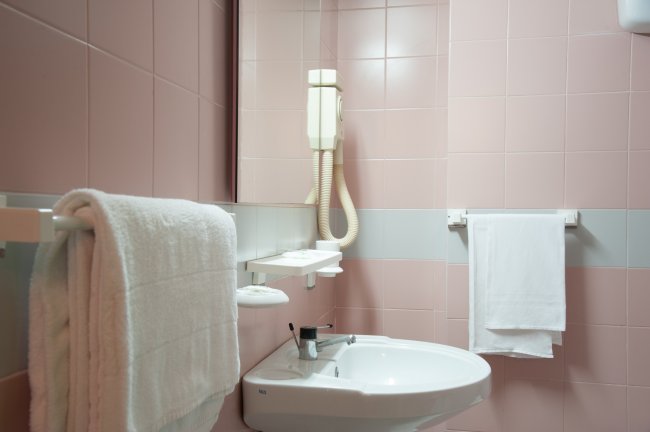 Bagno rosa con asciugacapelli e lavandino.
