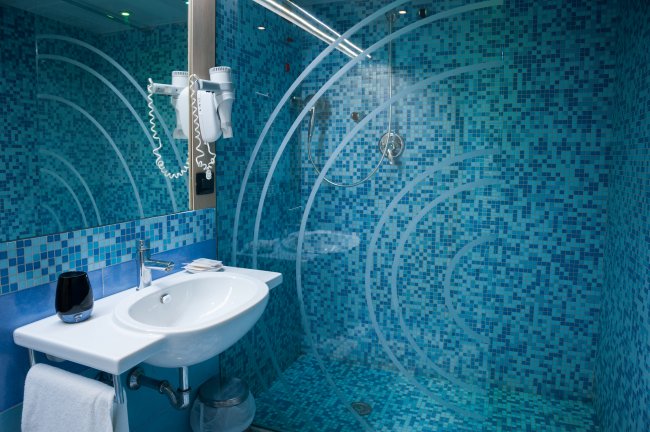 Bagno moderno con piastrelle blu e doccia in vetro.