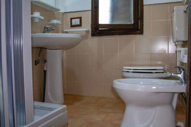 Una piccola stanza da bagno con lavandino, vaso e bidet. Piastrelle beige e finestra opaca.