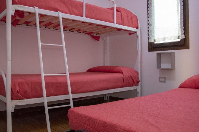 Camera con un letto a castello e un letto singolo, lenzuola rosse, finestra.