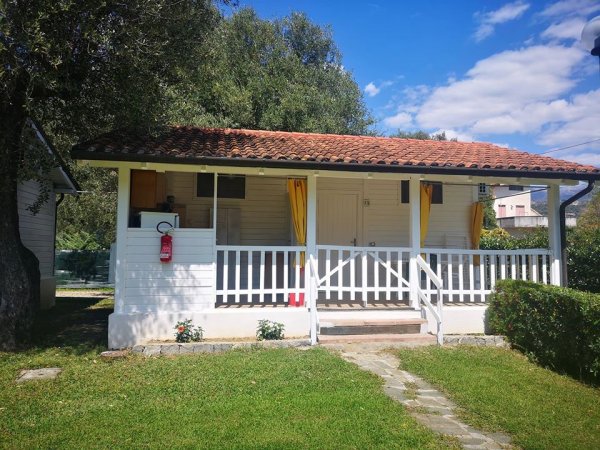 Piccola casa bianca con veranda, tetto rosso e prato curato davanti.