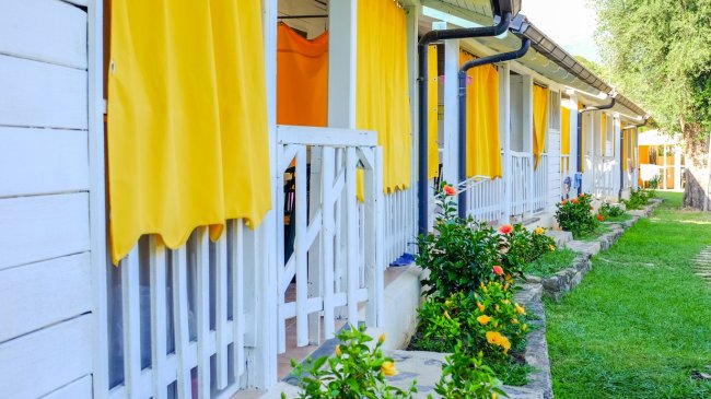 Filas di bungalow bianchi con tende gialle e fiori di fronte.