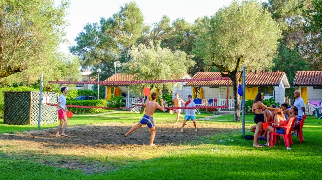 Ragazzi giocano a badminton su un campo all'aperto con spettatori seduti su sedie rosse.