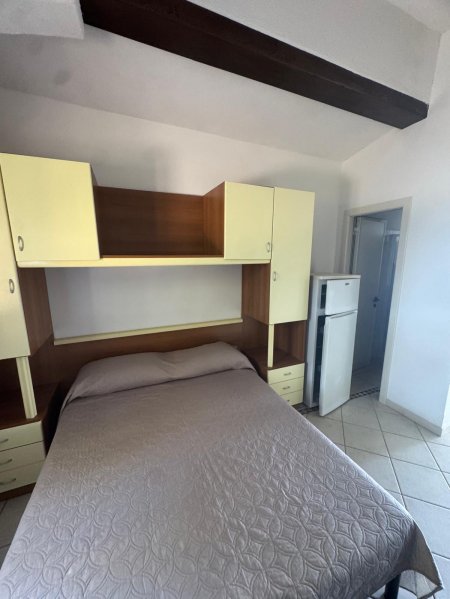 Letto matrimoniale sotto mensole, frigorifero vicino.
