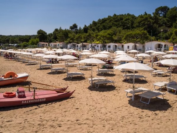 Spiaggia con lettini, ombrelloni bianchi e barca di salvataggio rossa.