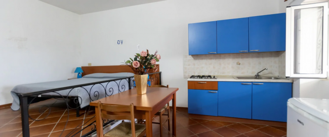 Monolocale con letto, cucina blu e tavolo con fiori.