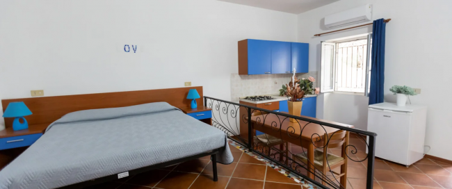 Monolocale con letto matrimoniale, cucina blu e tavolo.