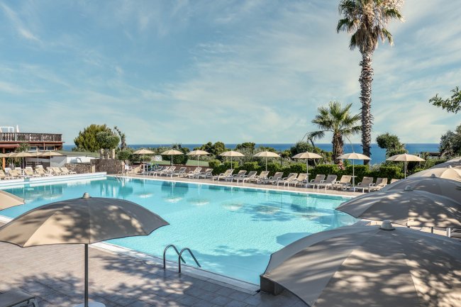 Piscina con lettini e ombrelloni, cielo sereno.