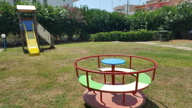 Parco giochi con scivolo giallo e giostra rotonda su erba.