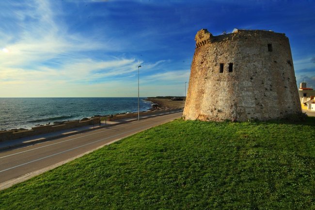 Una torre di pietra accanto a una strada costiera, con il mare sullo sfondo.