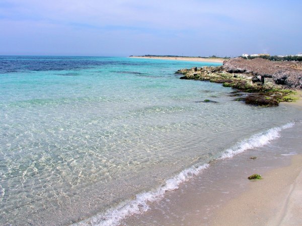 Spiaggia di sabbia chiara con acque limpide e onde leggere.