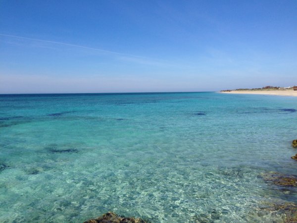 Mare cristallino e spiaggia sabbiosa sotto un cielo blu.