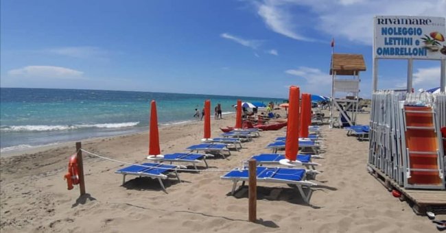 Spiaggia con ombrelloni e sdraio azzurri allineati a destra.