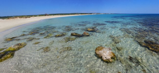 Una spiaggia con acqua cristallina e rocce sparse sotto un cielo blu.