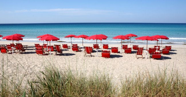 Ombrelloni e lettini rossi su una spiaggia sabbiosa con mare blu.