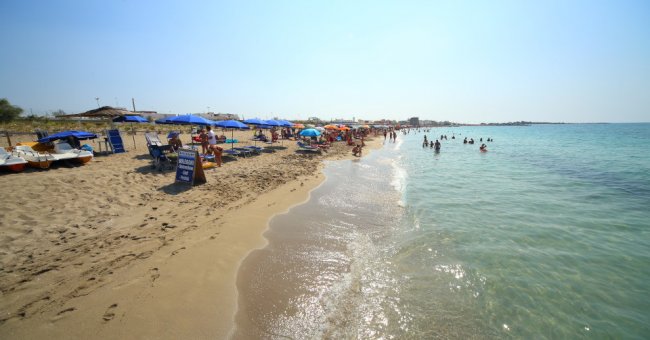 Spiaggia sabbiosa con ombrelloni blu e persone in acqua.