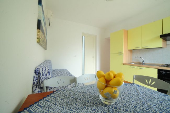 Cucina moderna con mobili gialli e tavola apparecchiata con tovaglia blu e ciotola di limoni.