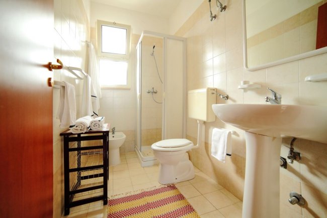 Bagno con doccia, wc e lavabo, tapppeto colorato.