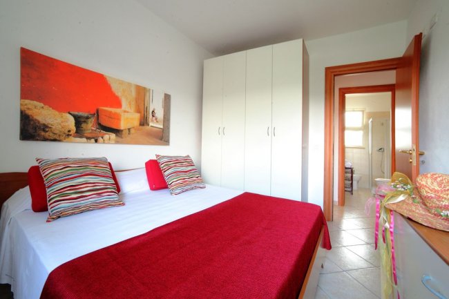 Camera da letto con copriletto rosso e quadri colorati.