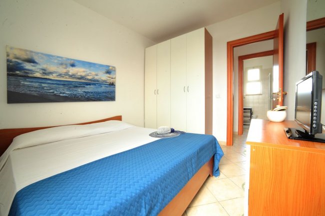 Una camera da letto con letto matrimoniale, copriletto blu e armadio bianco.