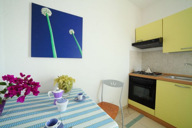 Una cucina con tavolo coperto da tovaglia a righe, fiori rosa e un quadro con fiori verdi.