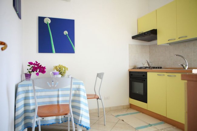 Cucina gialla con tavolino, sedie e quadro floreale blu.