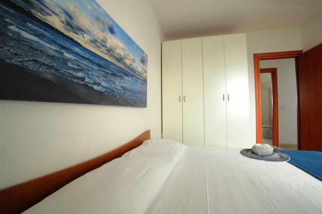 Camera da letto con letto matrimoniale, un armadio bianco e un quadro del mare appeso sopra.