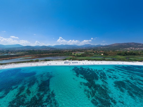 Spiaggia con mare turchese e montagne sullo sfondo.
